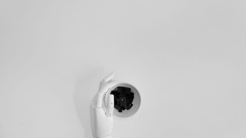 A robotic hand grasping black keyboard keys in a minimalist setting