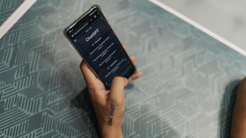 Close-up of a person holding a smartphone displaying the ChatGPT application interface on a patterned table