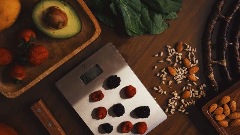 Top view of composed raw almond with seeds and avocado on table with berries on scales for cooking healthy...