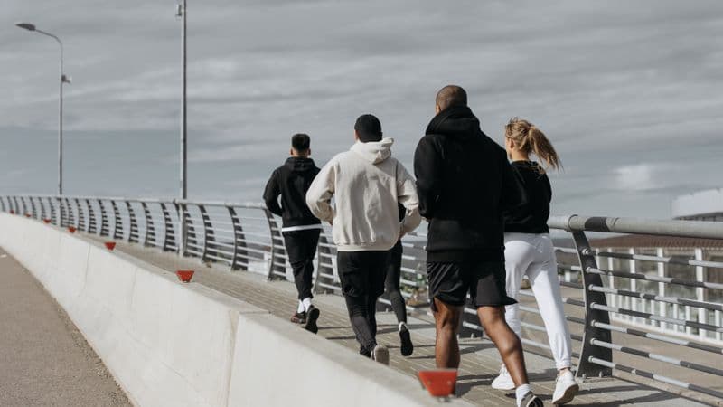 A diverse group of adults jogging together on a city bridge during the day