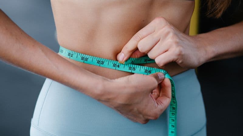 Close-up of a woman measuring her waist with a tape, representing fitness, health, and weight loss
