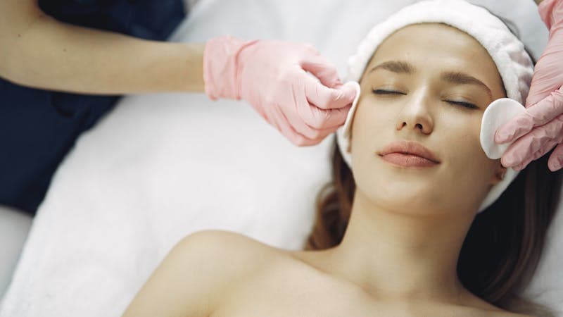 Close-up of skincare products being applied with dropper and cream jar